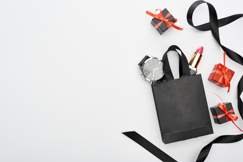 vista superior de la pequeña bolsa de compras con reloj de pulsera masculino y lápiz labial femenino cerca de la cinta y regalos sobre fondo blanco
 - Foto, Imagen