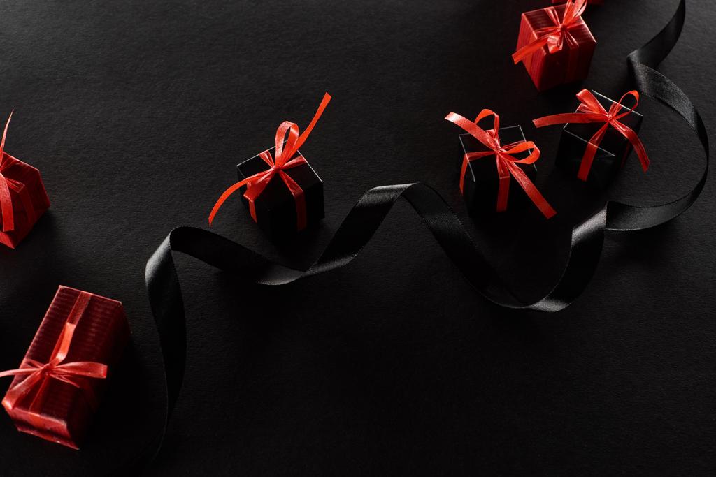 top view of black and red decorative gift boxes with bows near ribbon on black background - Photo, Image