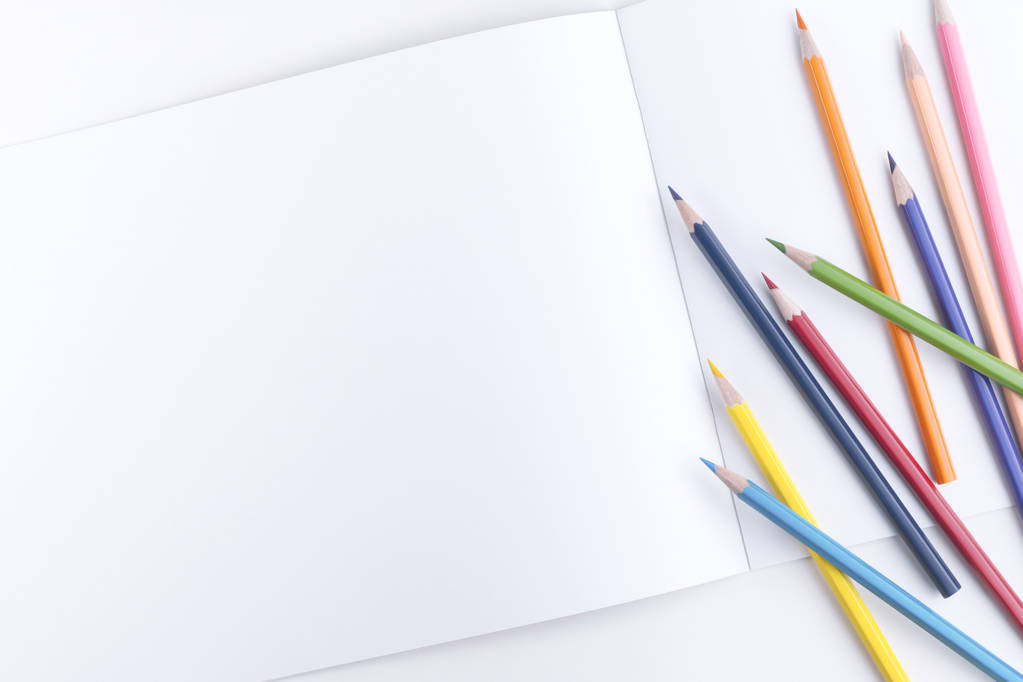 Set plano de lápices afilados multicolores esparcidos en un cuaderno abierto con páginas vacías sobre un fondo blanco
 - Foto, imagen
