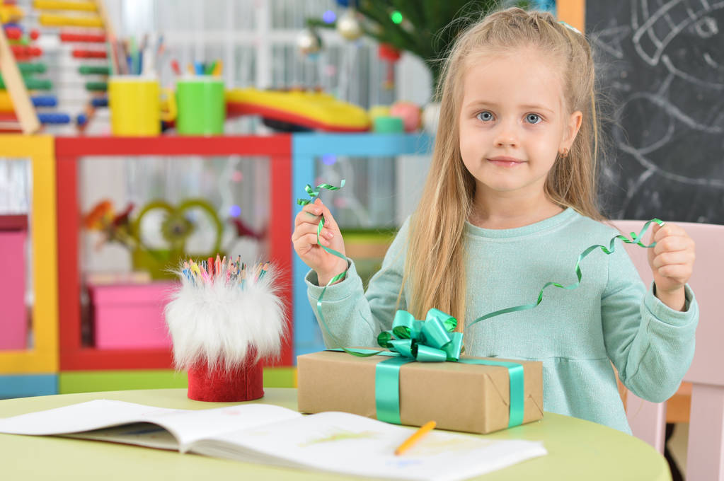 мила дівчина сидить за столом з подарунком
 - Фото, зображення