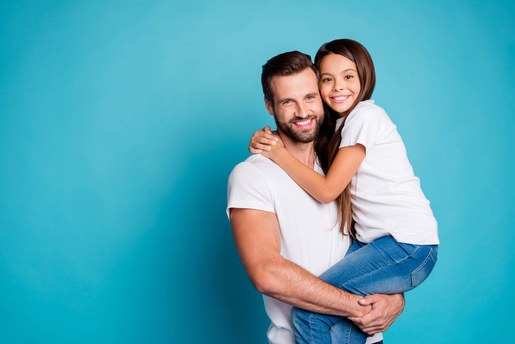 Portret van mooie man met Brunet haar knippen houden van zijn dochter hebben lang haar dragen witte casual t-shirt denim jeans geïsoleerd over blauwe achtergrond - Foto, afbeelding
