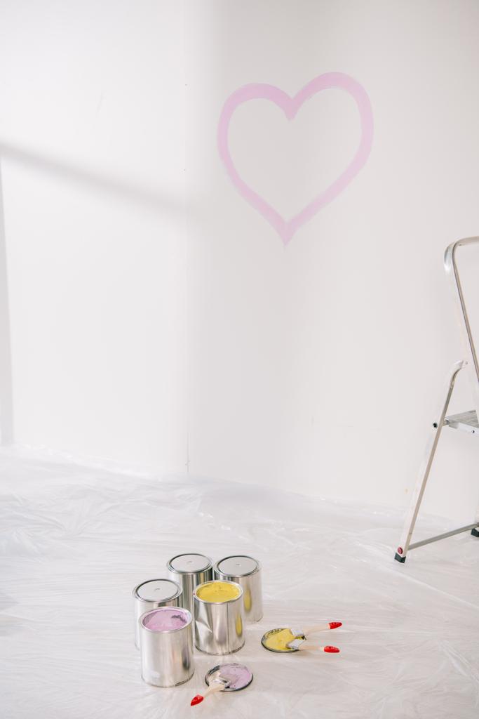 chambre avec coeur rose dessiné sur mur blanc, canettes avec peinture et pinceaux sur plancher blanc recouvert de cellophane
 - Photo, image