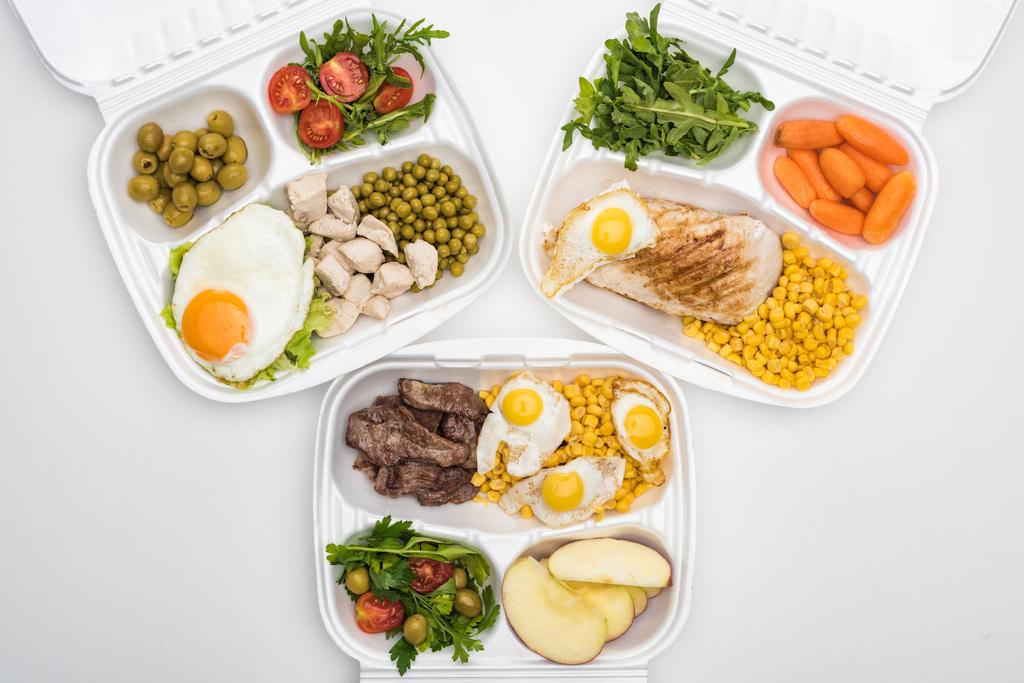 vista superior de pacotes ecológicos com maçãs, legumes, carne, ovos fritos e saladas em fundo branco
  - Foto, Imagem