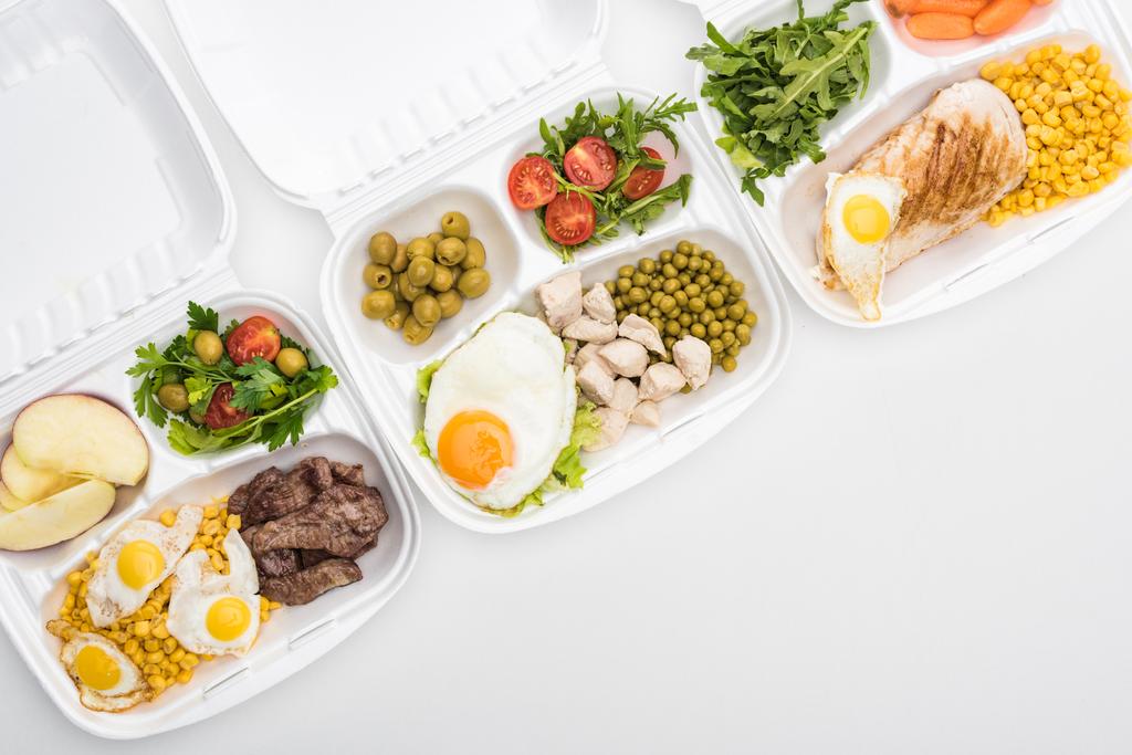vue du dessus des emballages écologiques avec pommes, légumes, viande, œufs frits et salades sur fond blanc
  - Photo, image