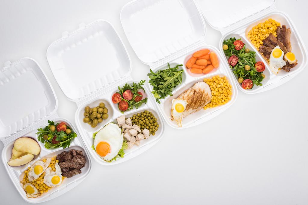 πάνω όψη των οικολογικών πακέτων με μήλα, λαχανικά, κρέας, τηγανητά αυγά και σαλάτες σε λευκό φόντο  - Φωτογραφία, εικόνα
