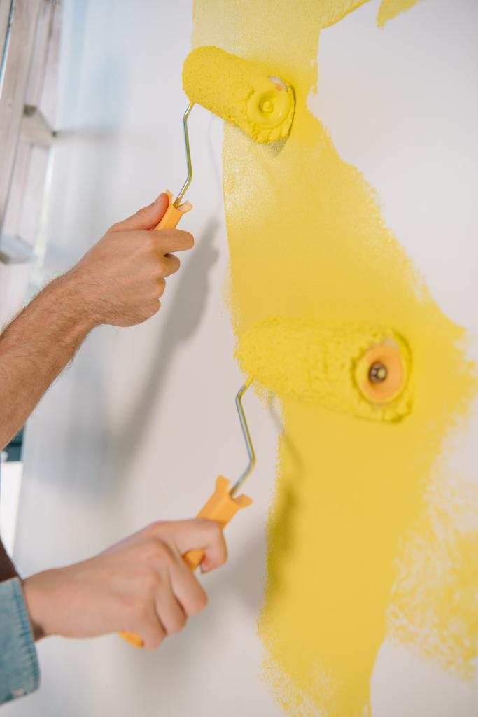 visão parcial do homem e da mulher parede de pintura em amarelo com rolos de pintura
 - Foto, Imagem