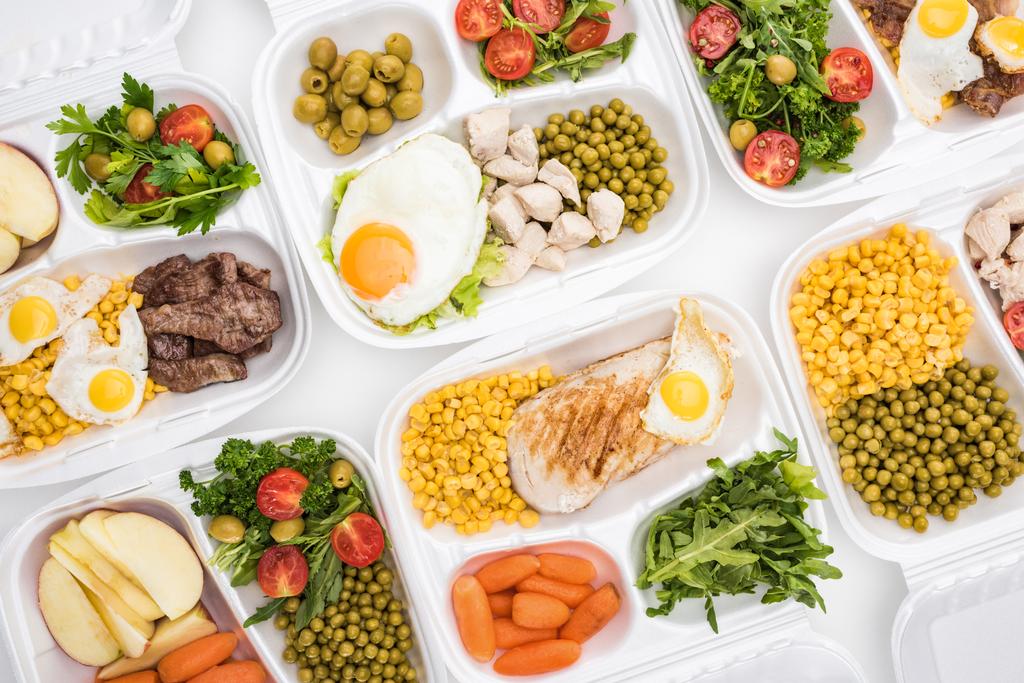 πάνω όψη των οικολογικών πακέτων με μήλα, λαχανικά, κρέας, τηγανητά αυγά και σαλάτες σε λευκό φόντο  - Φωτογραφία, εικόνα