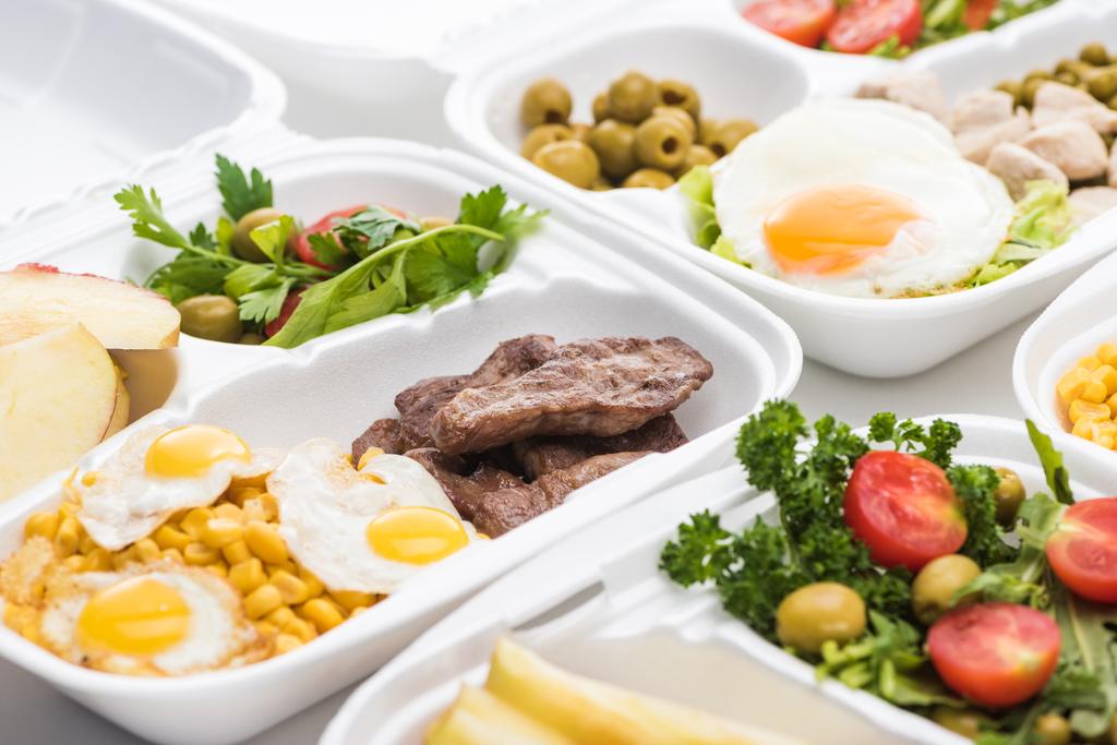 enfoque selectivo de eco paquete con ensalada, manzanas, huevos fritos y carne sobre fondo blanco
  - Foto, Imagen