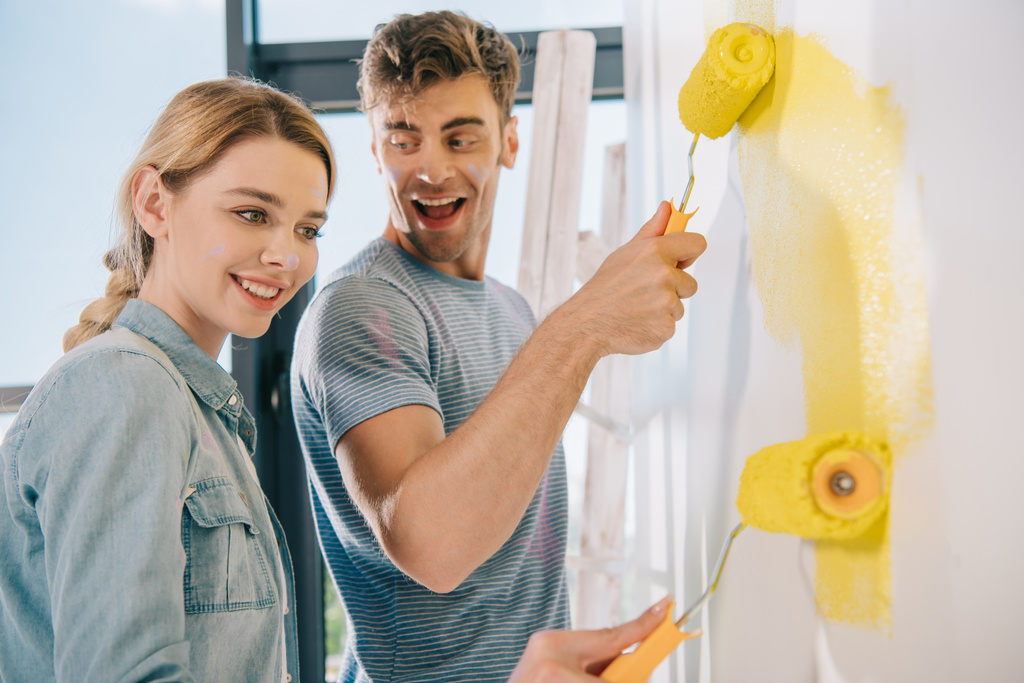 fröhliches junges Paar bemalt Wand in Gelb mit Farbwalzen - Foto, Bild