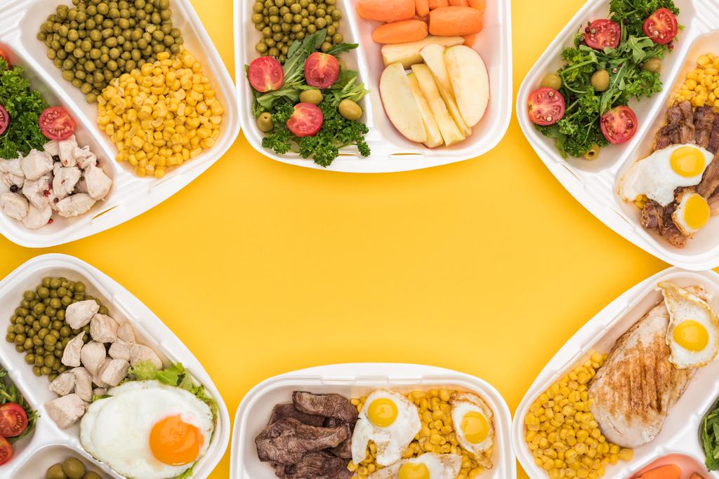 vista dall'alto di confezioni ecologiche con mele, verdure, carne, uova fritte e insalate isolate su giallo
  - Foto, immagini
