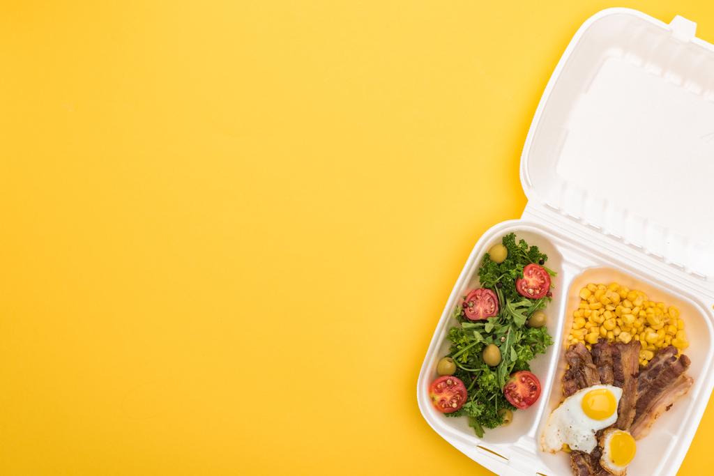 トウモロコシ、肉、目玉焼き、黄色のサラダが付いたエコパッケージの上からの眺め  - 写真・画像