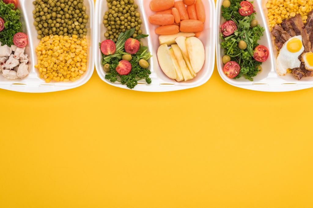 az almával, zöldségekkel, hússal, tükörtojással és sárgán izolált salátákkal ellátott ökocsomagok felülnézete  - Fotó, kép