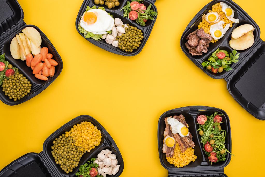 κορυφαία άποψη των οικολογικών συσκευασιών με μήλα, λαχανικά, κρέας, τηγανητά αυγά και σαλάτες που απομονώνονται στο κίτρινο  - Φωτογραφία, εικόνα