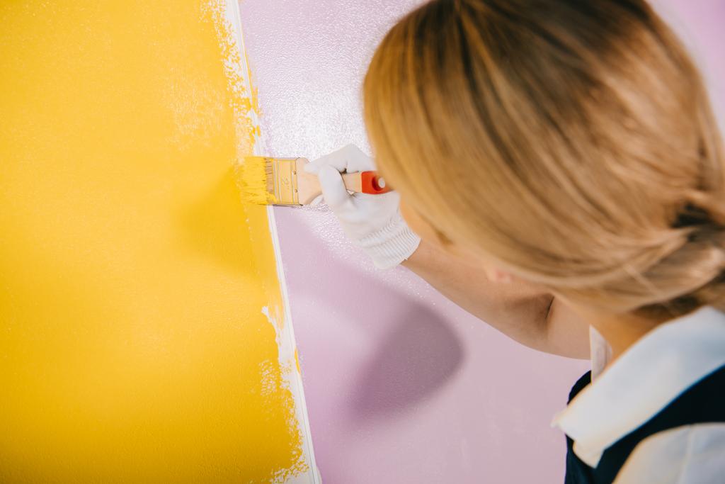 πίσω όψη του νεαρού ζωγράφου τοίχο ζωγραφικής σε κίτρινο και ροζ χρώμα με πινέλο - Φωτογραφία, εικόνα