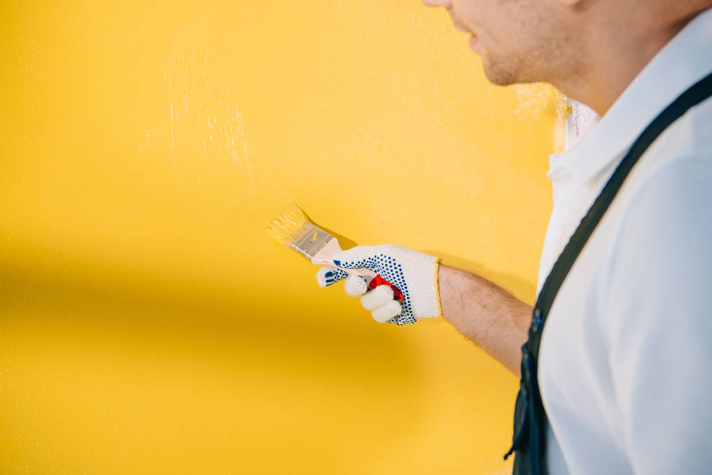 oříznutý pohled na mladého malíře malířské stěny ve žluté barvě s štětcem - Fotografie, Obrázek