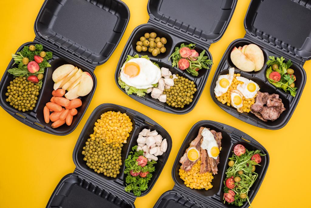 κορυφαία άποψη των οικολογικών συσκευασιών με μήλα, λαχανικά, κρέας, τηγανητά αυγά και σαλάτες που απομονώνονται στο κίτρινο  - Φωτογραφία, εικόνα
