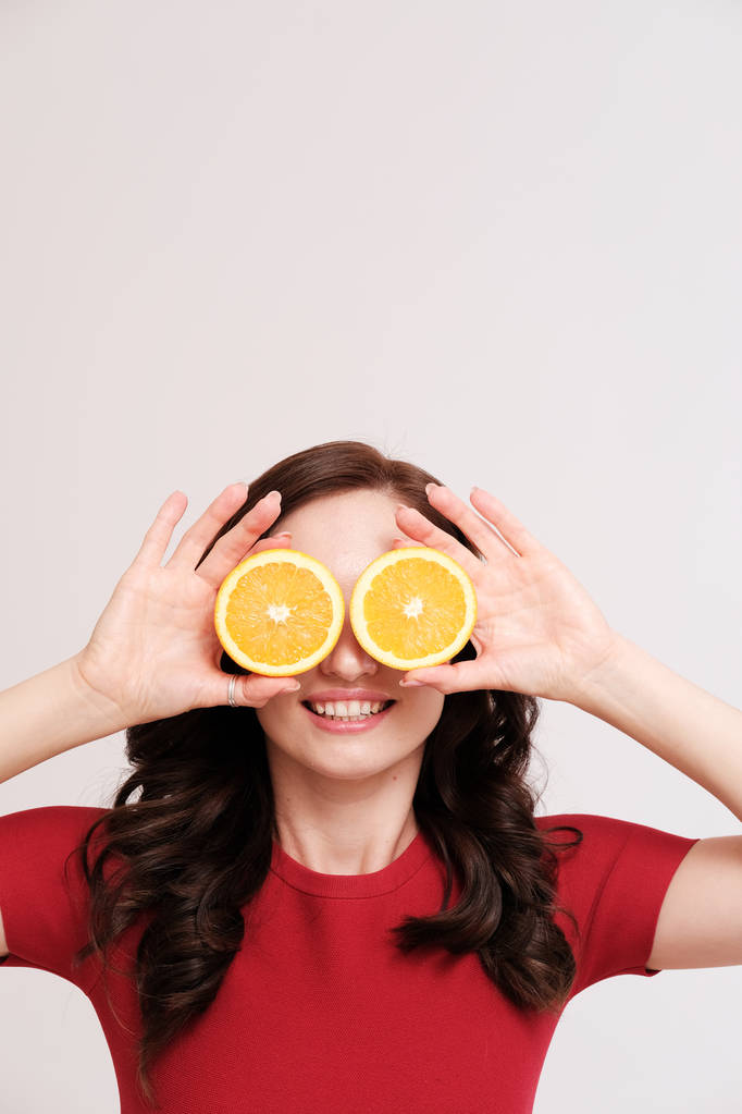 retrato de estúdio de jovem morena com laranjas cobrindo olhos em fundo liso
 - Foto, Imagem