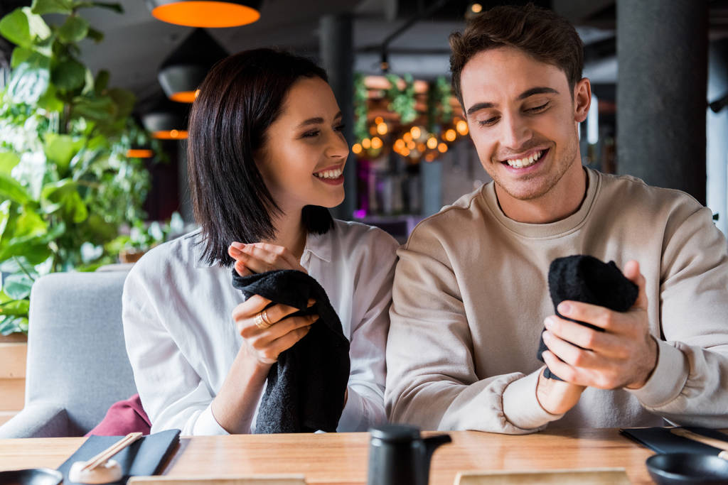cheerful man and happy woman holding black napkins in sushi bar  - 写真・画像