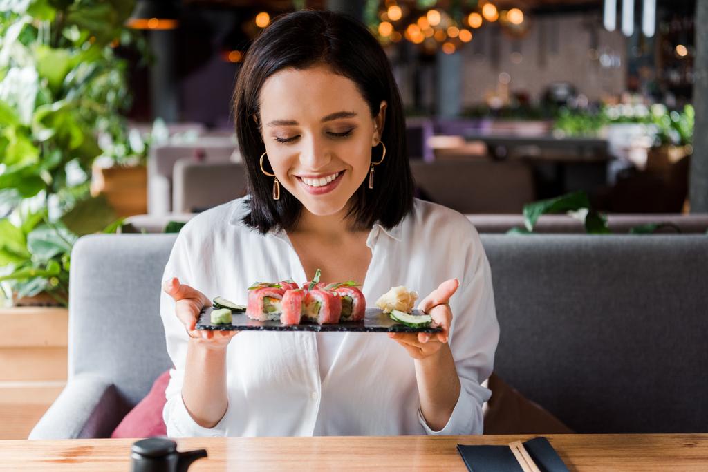 ευτυχισμένη γυναίκα κρατώντας πιάτο με νόστιμο σούσι στο εστιατόριο  - Φωτογραφία, εικόνα