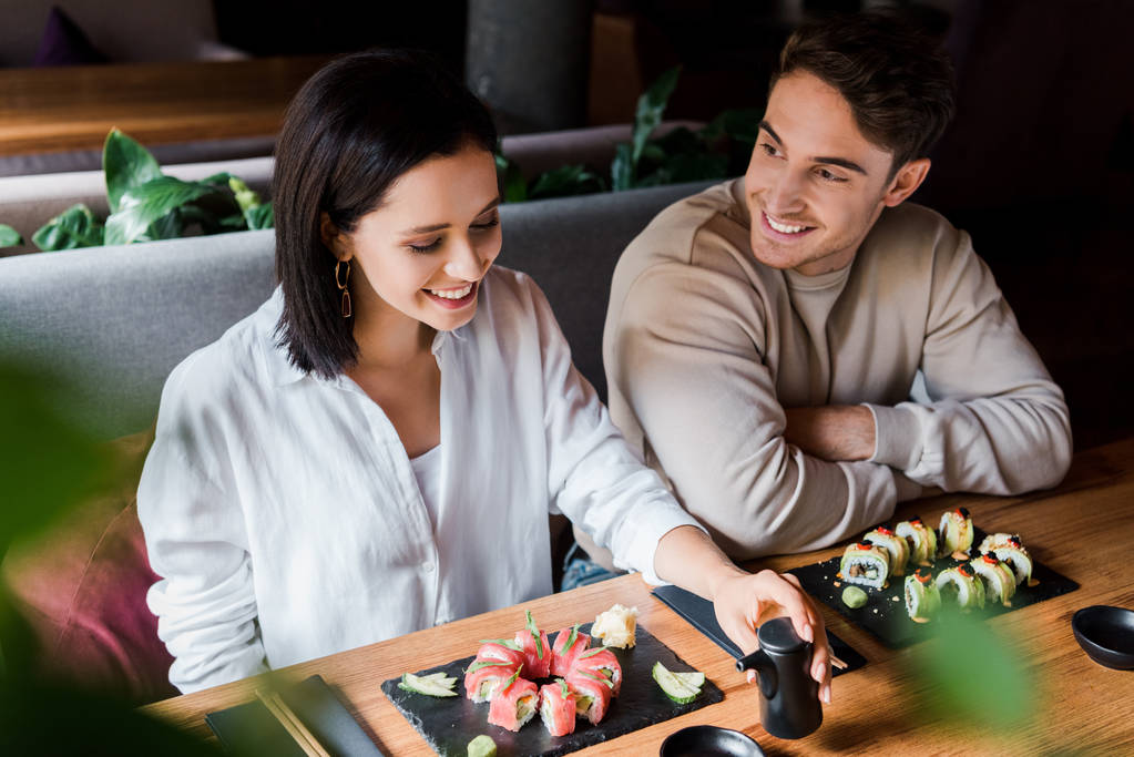 избирательный фокус счастливого мужчины, смотрящего на веселую женщину, улыбающуюся рядом с тарелками с суши
  - Фото, изображение