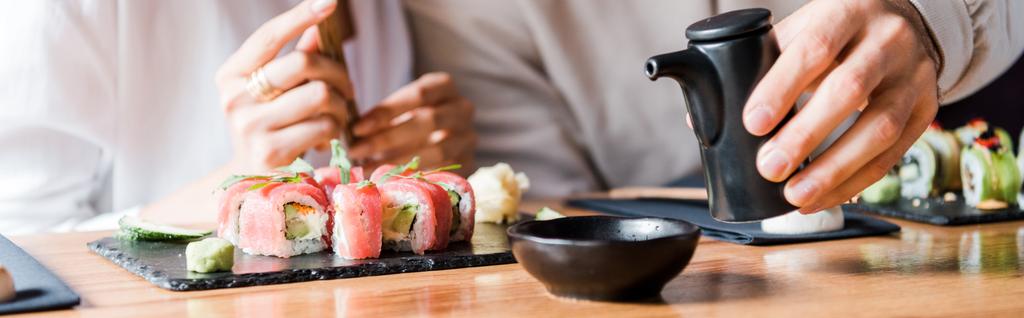 tiro panorâmico de homem segurando garrafa preta perto de mulher e sushi
  - Foto, Imagem