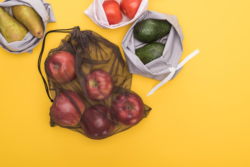 vista superior de manzanas maduras, peras, tomates, aguacate en bolsas ecológicas aisladas en amarillo
 - Foto, Imagen