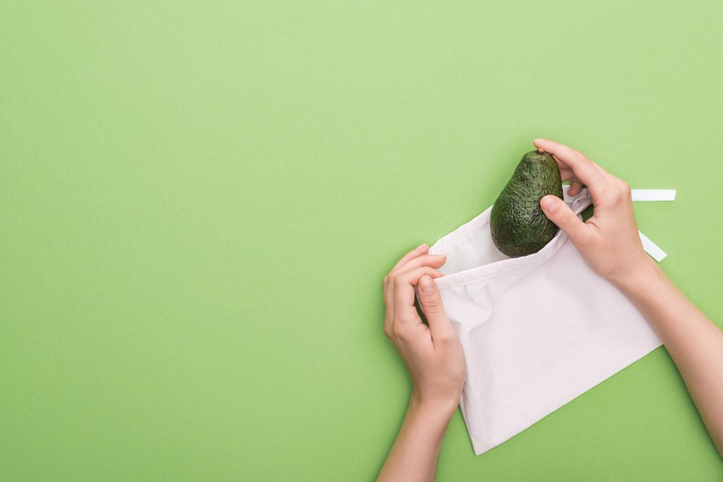 vista cortada da mulher colocando abacate em saco ecológico isolado no verde
 - Foto, Imagem
