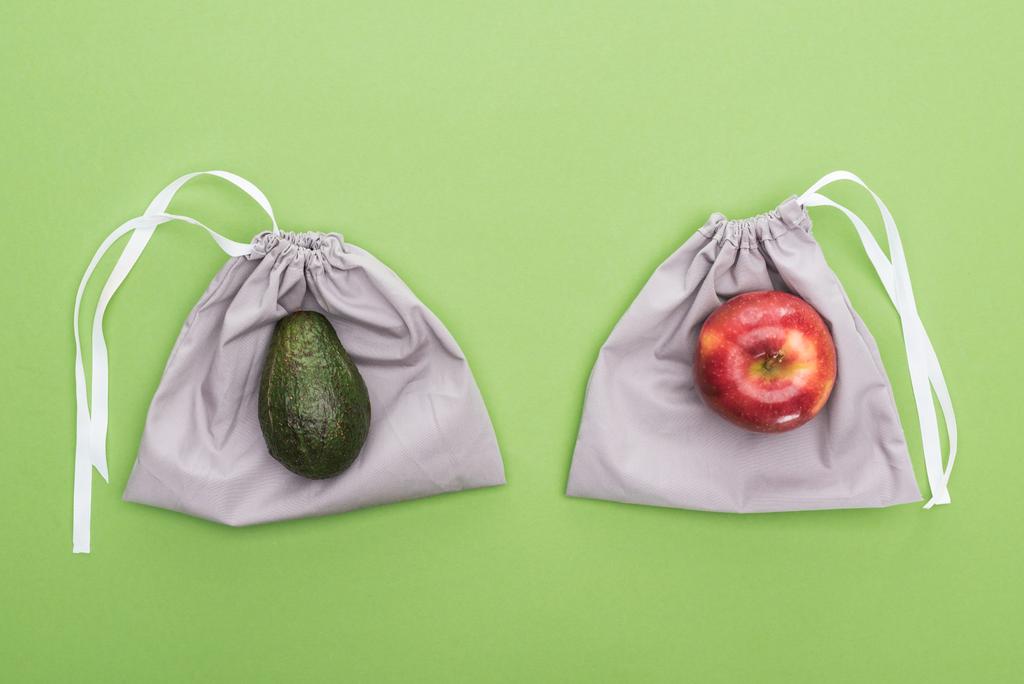 Κορυφαία θέα του αβοκάντο και της Μήλου σε φιλικές προς το οικολογικό σακούλες απομονώνονται σε πράσινο - Φωτογραφία, εικόνα