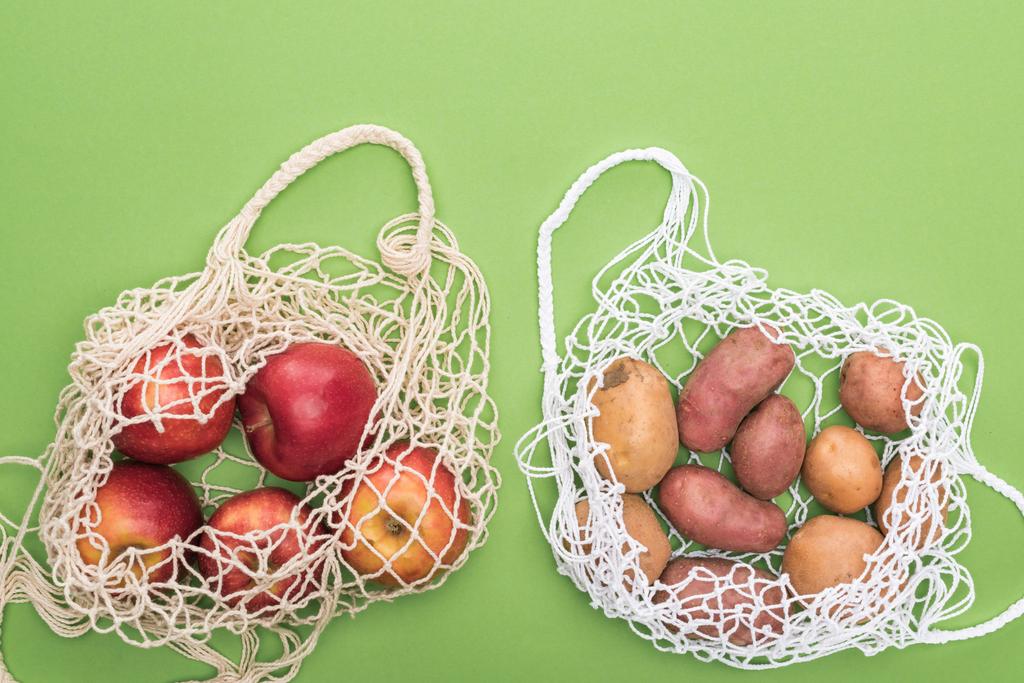 top view of ripe apples and potatoes in string bags isolated on green - Photo, Image