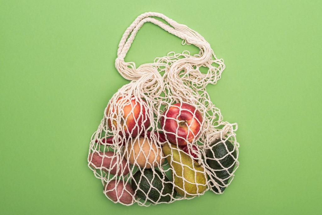 Blick von oben auf Gemüse und Obst in Schnur Tasche isoliert auf grün - Foto, Bild