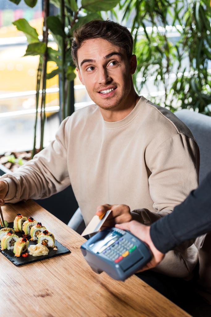 selective focus of handsome man holding credit card near credit card reader  - Photo, Image