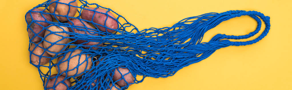 Κορυφαία θέα των πατατών σε μπλε τσάντα string απομονωθεί σε κίτρινο, πανοραμική βολή - Φωτογραφία, εικόνα