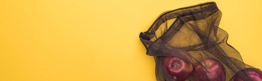 верхний вид яблок в экологически чистой черной сетке мешок изолирован на желтый, панорамный снимок
 - Фото, изображение