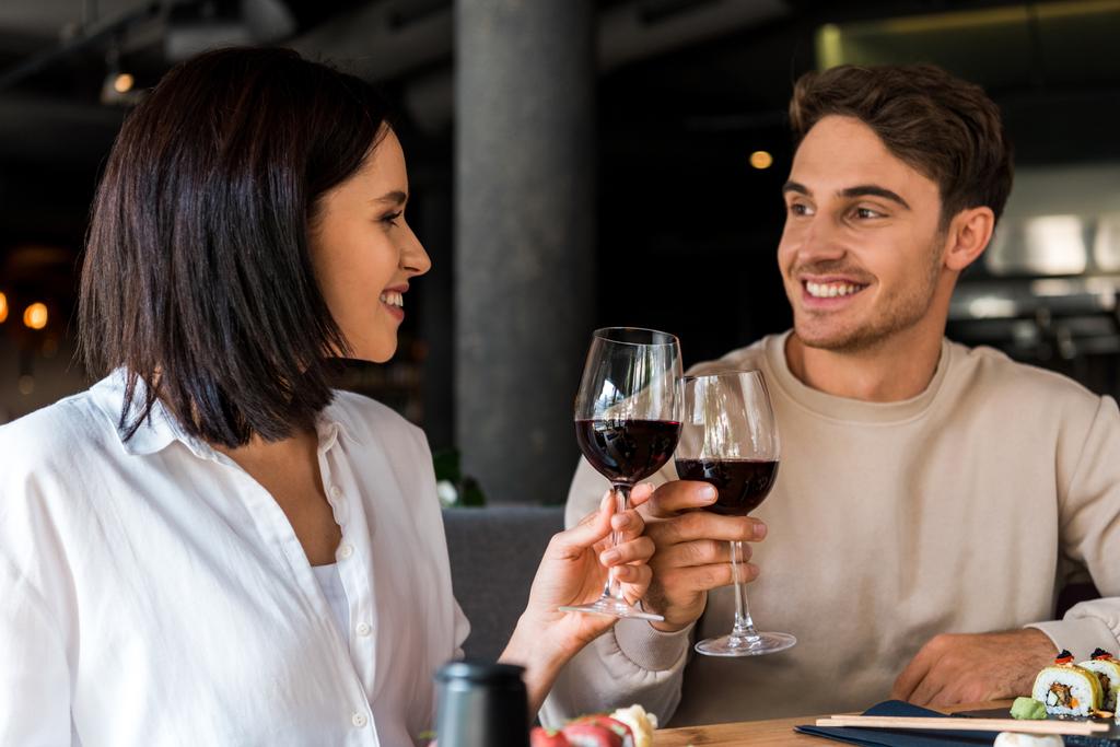 Ευτυχισμένος άντρας και χαρούμενη γυναίκα, γυαλίζει με κόκκινο κρασί κοντά στο σούσι.  - Φωτογραφία, εικόνα