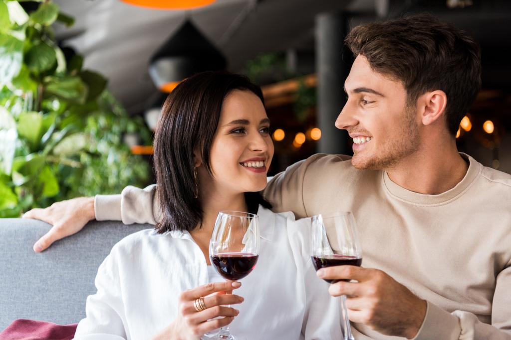Ευτυχισμένος άντρας και χαρούμενη γυναίκα κρατώντας ποτήρια με κόκκινο κρασί  - Φωτογραφία, εικόνα