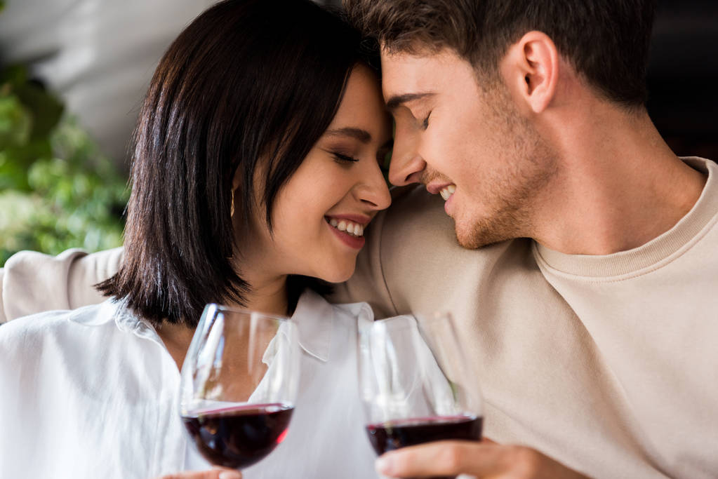 happy man and cheerful woman with closed eyes holding glasses with red wine  - Photo, Image