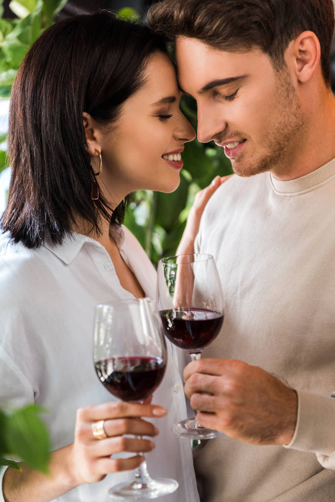 Selektiver Fokus des glücklichen Mannes, der ein Glas mit Rotwein in der Nähe des schönen Mädchens hält  - Foto, Bild
