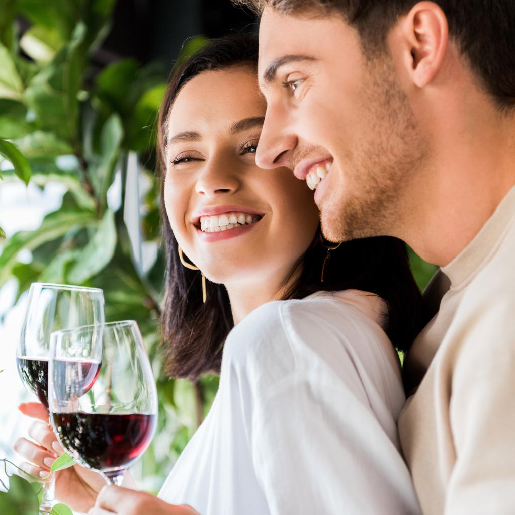 счастливый мужчина держит бокал с красным вином рядом с красивой девушкой
  - Фото, изображение