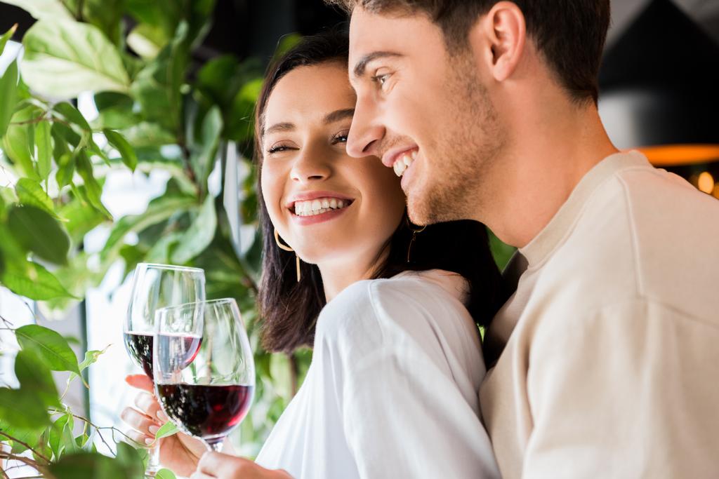 selectieve focus van knappe man met glas met rode wijn in de buurt van mooi meisje  - Foto, afbeelding