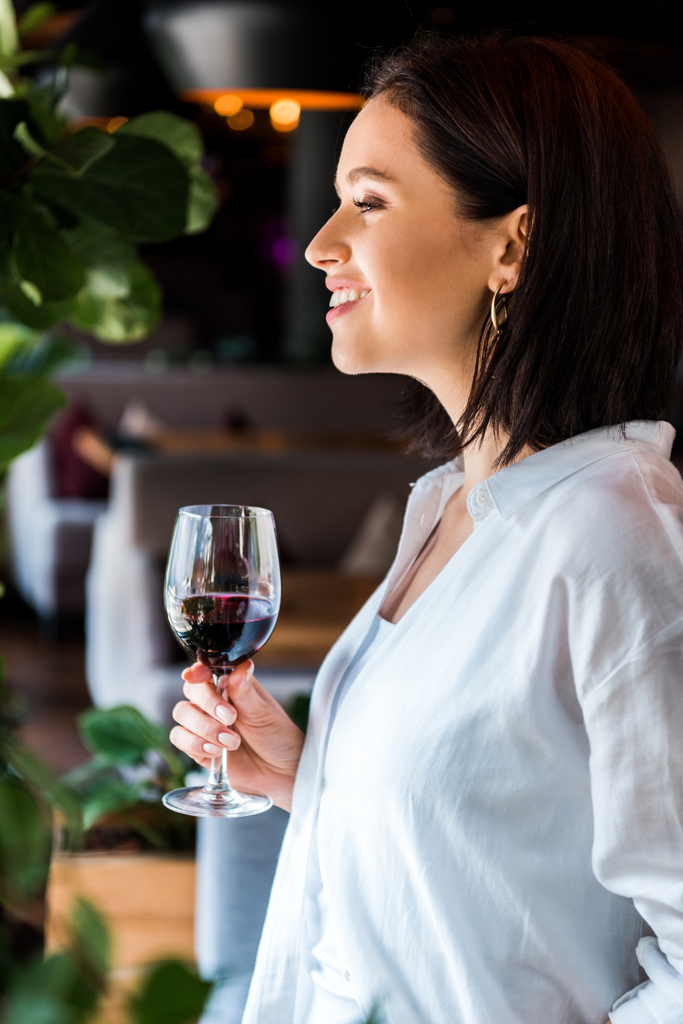 zijaanzicht van vrolijke vrouw met glas met rode wijn  - Foto, afbeelding