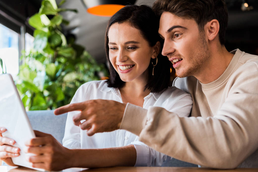 boldog férfi ujjal mutogatott laptop közelében nő étteremben  - Fotó, kép