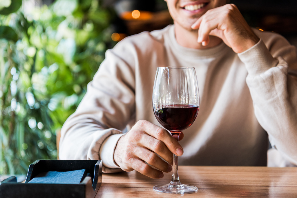 przycięty widok wesoły człowiek siedzi w restauracji ze szklanką wina  - Zdjęcie, obraz