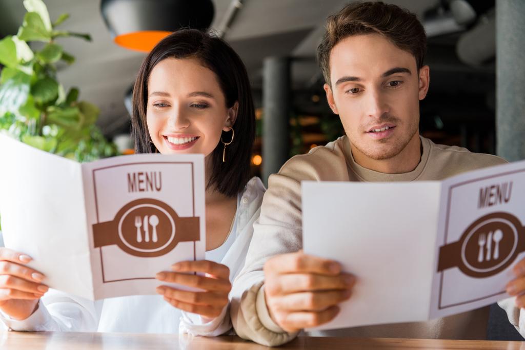 selective focus of happy man and smiling woman looking at menus in restaurant  - Photo, Image