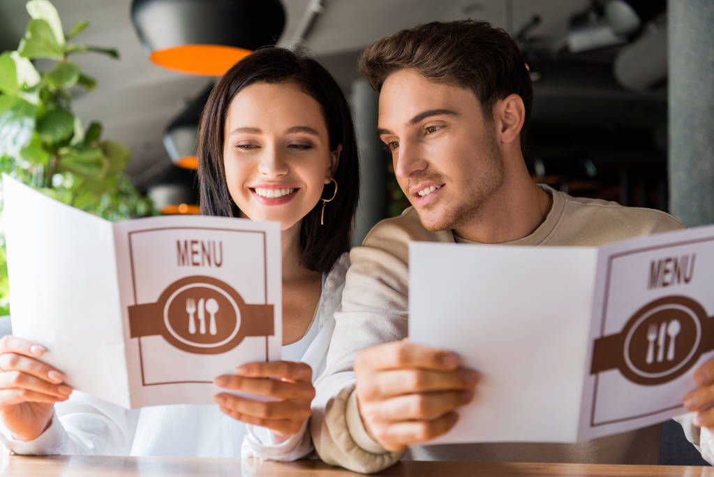 selectieve focus van man en gelukkige vrouw op menu 's in restaurant  - Foto, afbeelding
