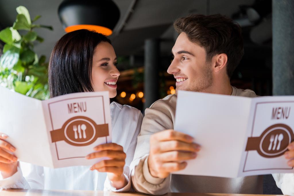 幸せな男女はレストランでメニューを持ちながらお互いを見ています  - 写真・画像