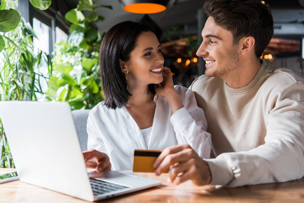 selectieve focus van vrolijke vrouw kijken naar man met creditcard in de buurt van laptop  - Foto, afbeelding