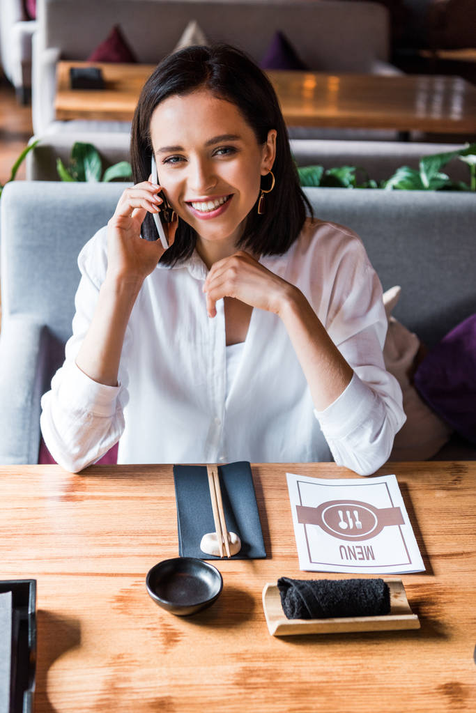 boldog nő beszél okostelefon közelében menü az asztalon  - Fotó, kép