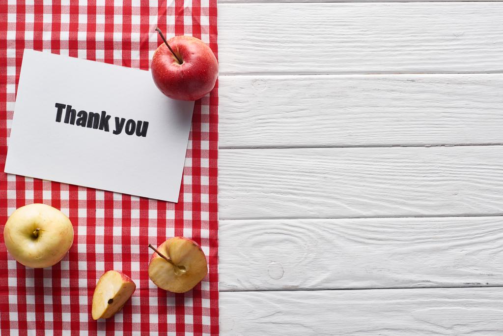 верхний вид спелых яблок и благодарственная открытка на деревянном белом столе с красной клетчатой салфеткой
 - Фото, изображение