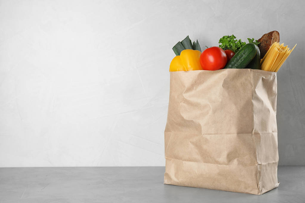 Χάρτινη σακούλα με φρέσκα λαχανικά σε γκρίζο τραπέζι με ανοιχτόχρωμο φόντο, Χώρος για κείμενο - Φωτογραφία, εικόνα