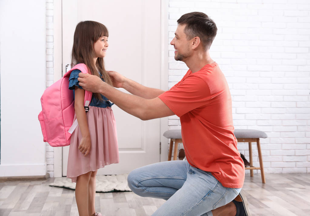 Ευτυχισμένος πατέρας βοηθώντας το μικρό παιδί του να βάλει στη σχολική τσάντα στο σπίτι - Φωτογραφία, εικόνα